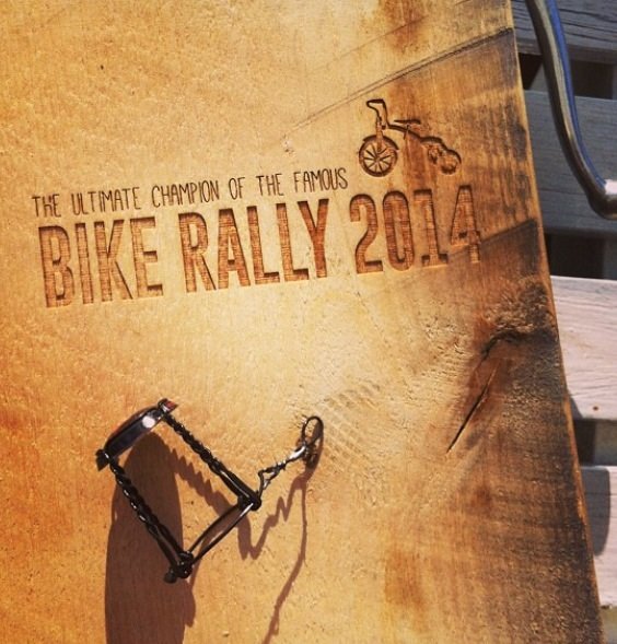 Træbræt med brændemærket tekst "Bike Rally 2014" og en cykelgrafik. En åbnet flaskeåbner ses ved siden af.