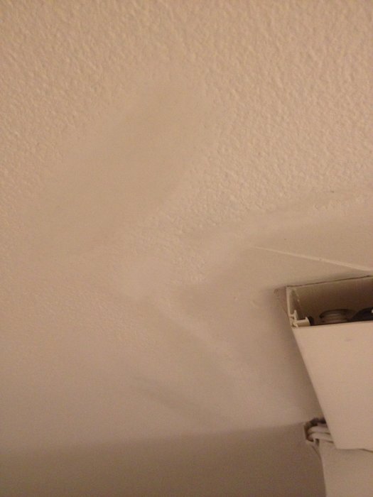 Image of a ceiling with a smooth plastered area amidst a textured surface, showing an issue with uneven plastering near a corner fixture.