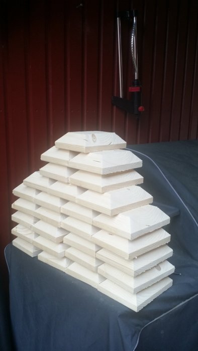 Stack of homemade wooden post caps on a dark surface against a red wall.