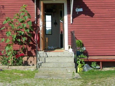 Steintrapp foran et rødt hus, omgitt av solsikker og planter.