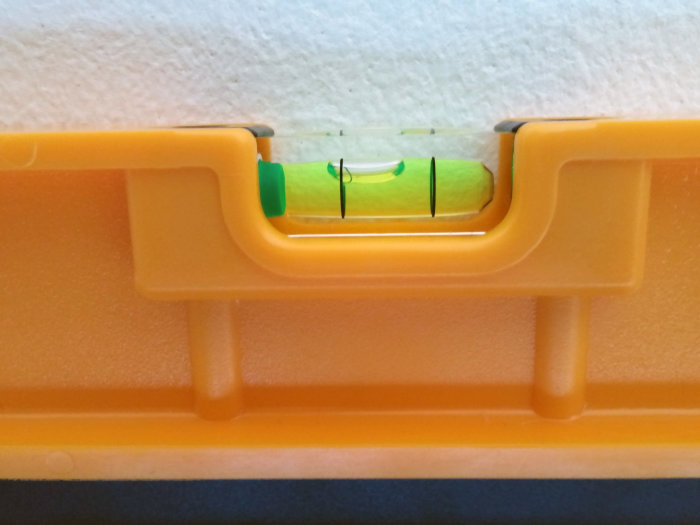 Et gult vaterpas på en overflade, hvor boblen ikke er centreret, viser ujævnhed eller skævhed.