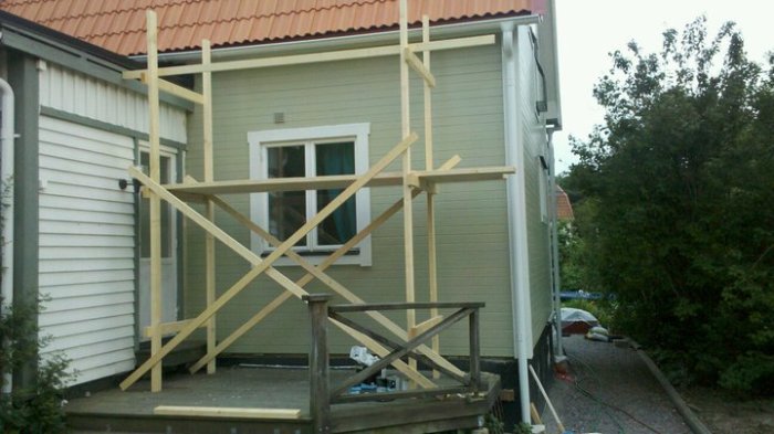 Wooden framework scaffolding built with 45x95 and 195x45 planks outside a house with a red roof and pale green siding.