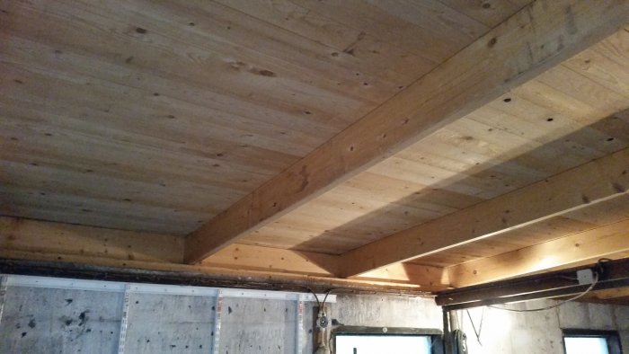 Wooden garage ceiling with visible beams. Ceiling boards are unstained and show grain. The garage is dimly lit with visible concrete walls below.