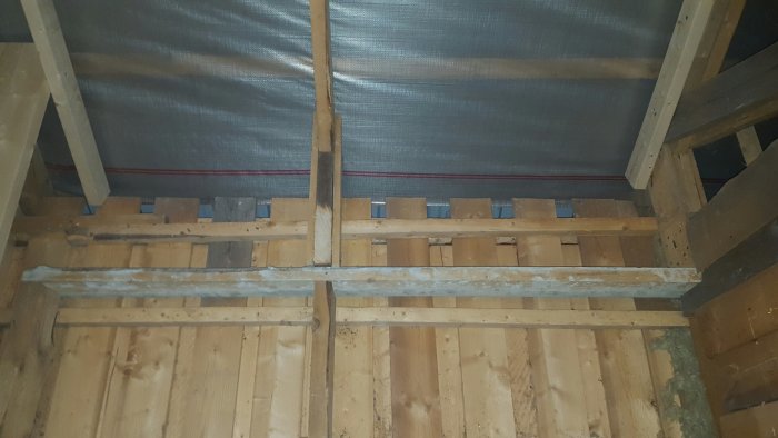 Interior of a wooden shed under renovation, showing rafters, wooden planks, and wall boards. Discussion about insulation and constructing eaves.