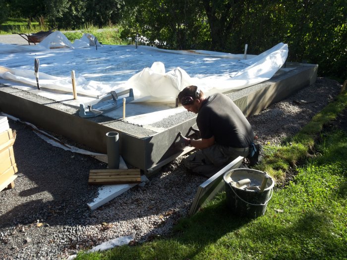 Person förbereder ytan för klinkerläggning på en nyligen gjuten betongplatta utomhus.