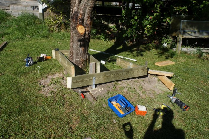 Anläggning av träbänk runt träd, med varierande djup för att omsluta rötter, och verktyg synliga.