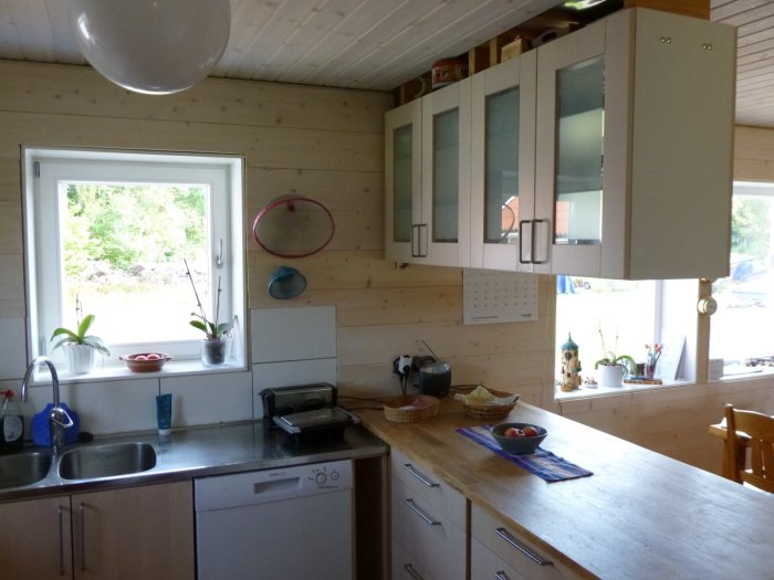 Använt kök med IKEA vitrinskåp, diskbänk från blocket och brödkorgar på bänken.