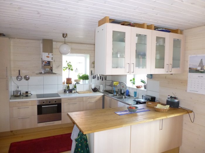 Ett verkligt använd kök med diskbänk, IKEA vitrinskåp, och en väggpanel med brödkorgar på bänken.