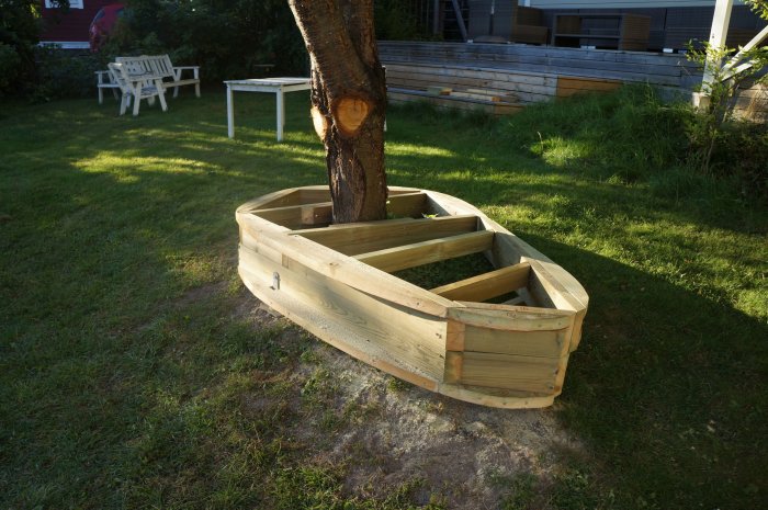 Träkonstruktion för salning placerad runt träd på en gräsmatta, i ett hushålls trädgård.