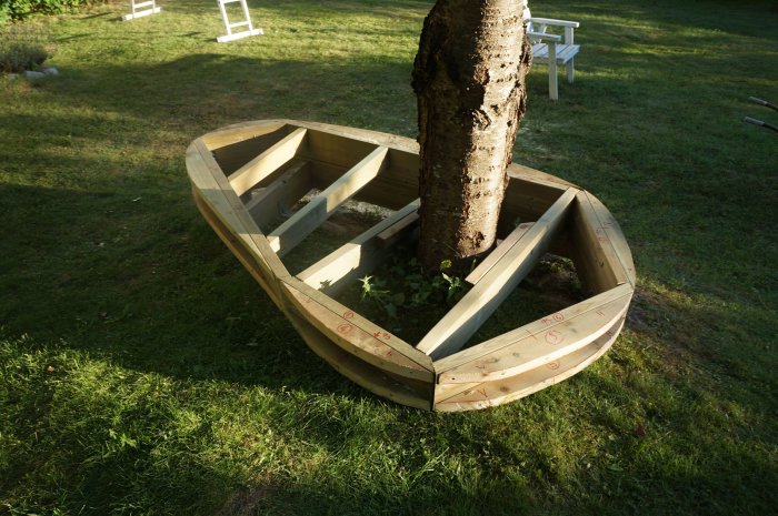 Oktagonformad träkonstruktion runt ett träd på en gräsmatta i förberedelse för salning.