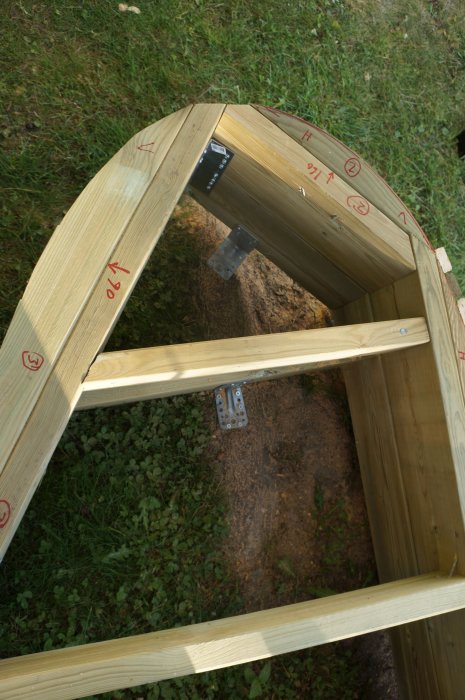 Byggkonstruktion av träbågar markerade för salning med metallbeslag i en trädgård.