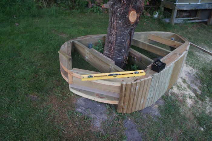 Halvfärdig träinklädnad runt träd, 45 x 45 mm reglar, vattenpass ovanpå, 1 cm mellanrum till marken.