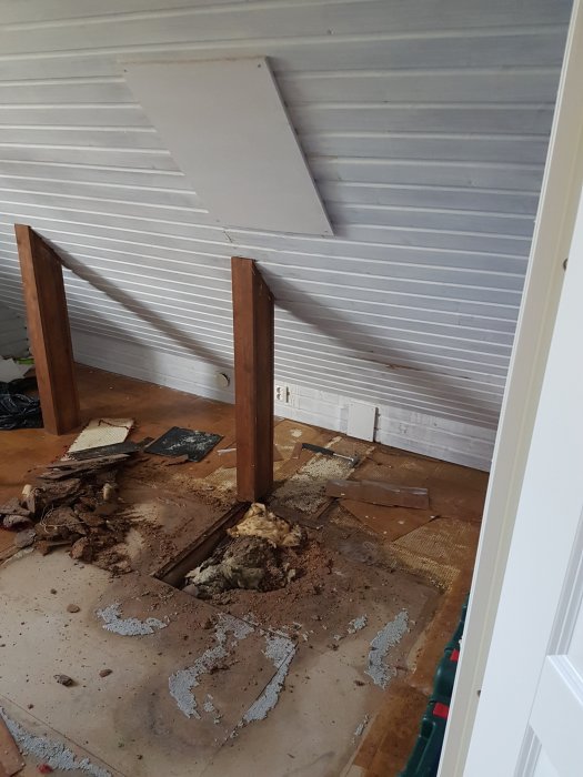Vattenskador på ovanvåningen med smulande spånskivor och missfärgad isolering, nära en borttagen skorsten.