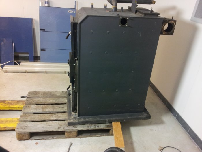 En varmepanna på en pall i ett verkstadsutrymme med röranslutningar och genomföringar redo för installation.