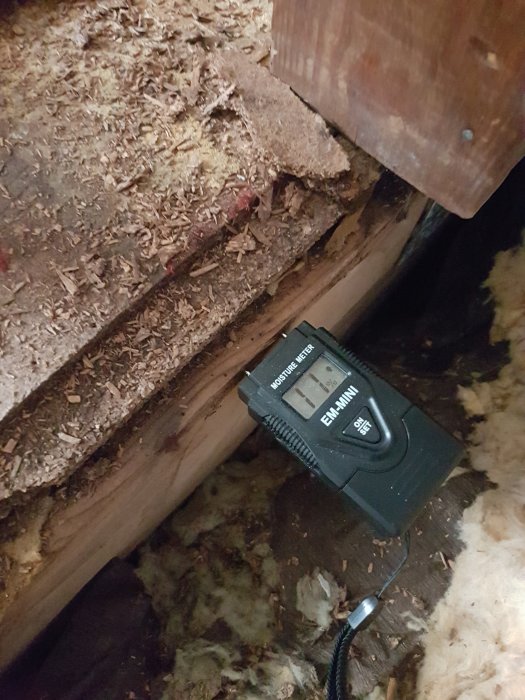 En fuktmätare på en träbalk med spånskivor indikerar fuktnivå i en byggnadsstruktur.