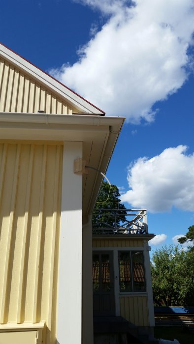 Nyligen målat hus i gult med vita knutar och en omonterad taklampa i förgrunden under en blå himmel med moln.