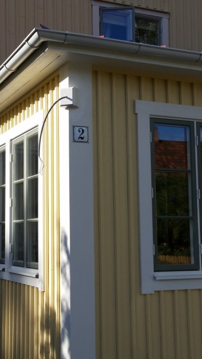 Nymålad yttervägg och fönsterkarmar på ett hus med gatunummer och avtäckt lampkabel.