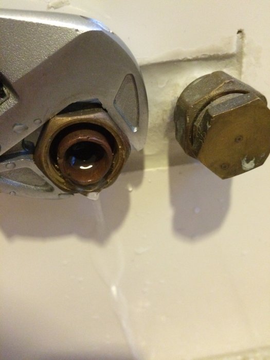 Närbild på rörmokarverktyg som håller en koppling bredvid en lossad mutter på vägg.