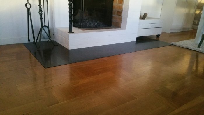 Mörkbrunt parkettgolv i ett vardagsrum med synlig spis och vitmålad golvsockel.