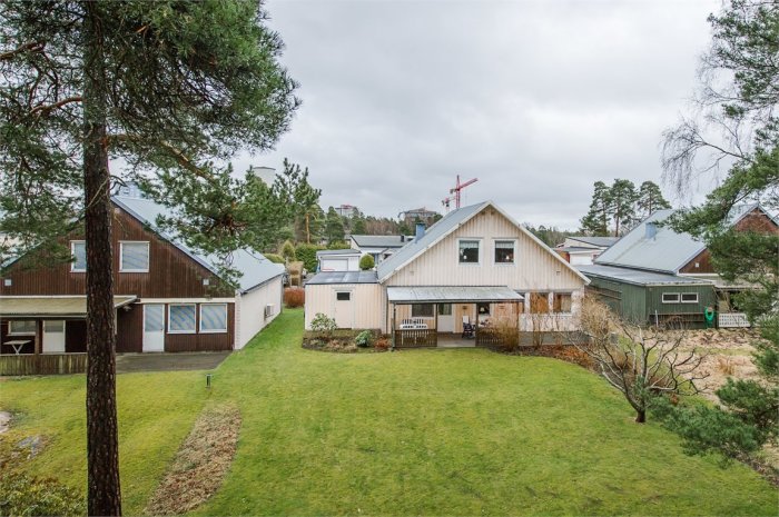 Trähus i två våningar med vit fasad och svart tak, omgivet av träd och gräsmatta i Skoghall, byggt 1972.