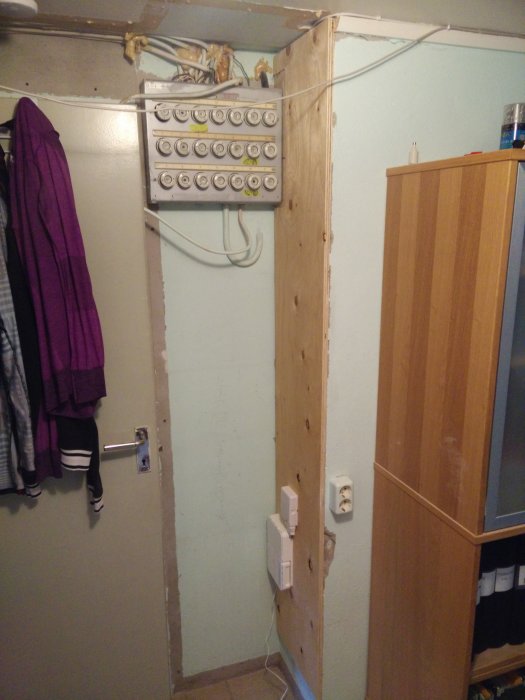 Gammal elcentral med sladdar och en träplanka i ett rum som är redo för renovering.