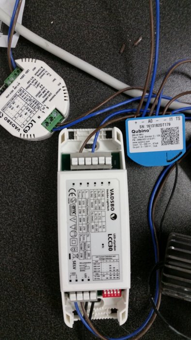 Elektriska komponenter för hemautomation, däribland en Qubino 0-10V dimmer och LED drivdon, på matta.