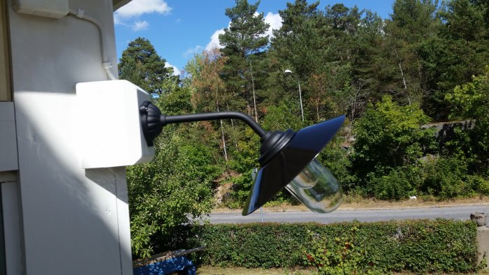 Nyinstallerad utomhuslampa på ett hus med vy mot en väg och grönskande landskap i bakgrunden.