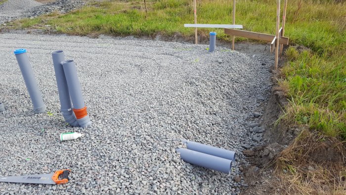 Grusgrund med rör och installationskomponenter för byggprojekt samt såg.