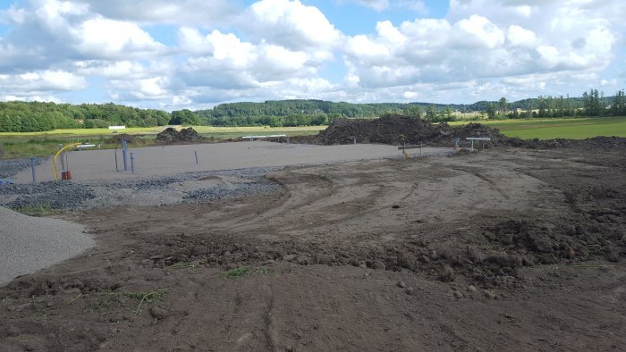 Byggplats i initialt skede med grävda schakt och markerade installationspunkter på en öppen yta.