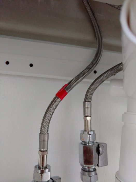 Nyinstallerade flexibla rörkopplingar under vask med tätning markerad i rött.