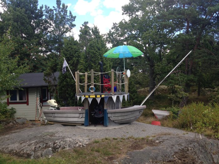 Hemmagjord barnlekplats formad som en båt gjord av återvunna material med en paraply och flagga.