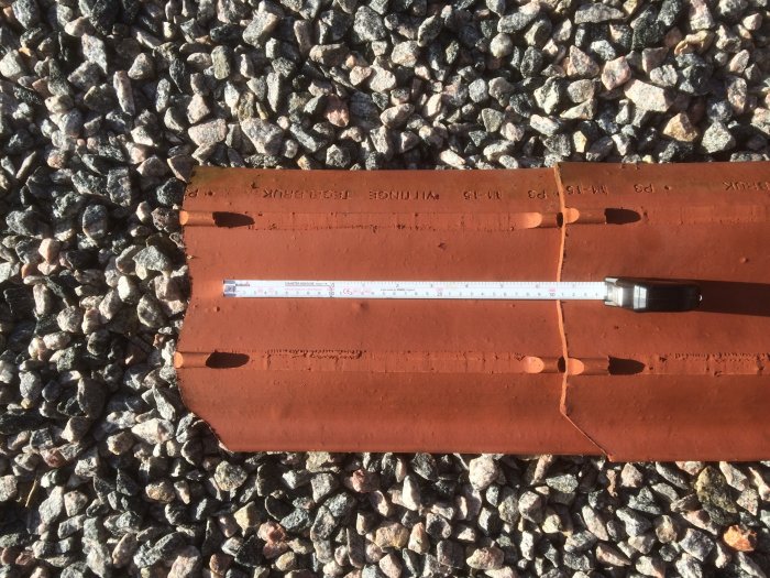 Mätning av läktavstånd på röda takpannor med måttband för byggprojekt.