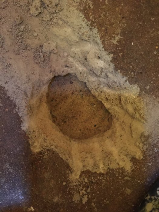 Hål i marken omgivet av hårdare material och sand, möjligen från erosion eller grävning.