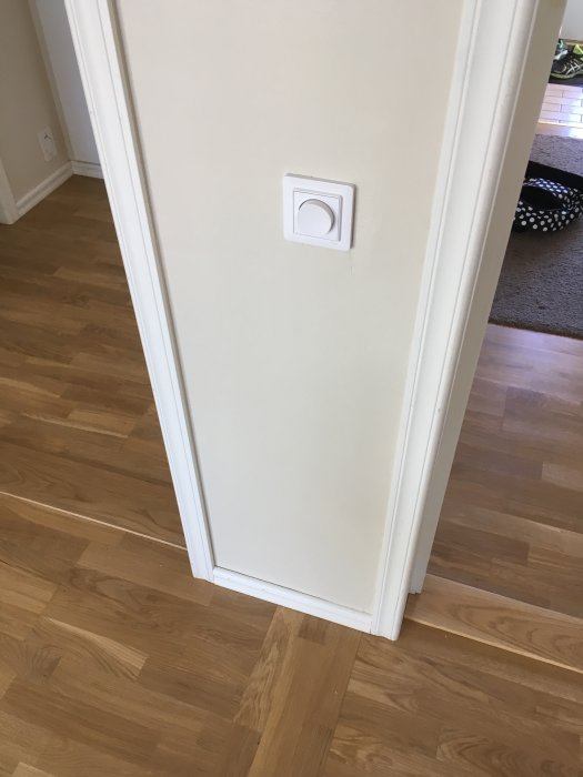 En strömbrytare på en vit dörrkarm med ett parkettgolv i bakgrunden.