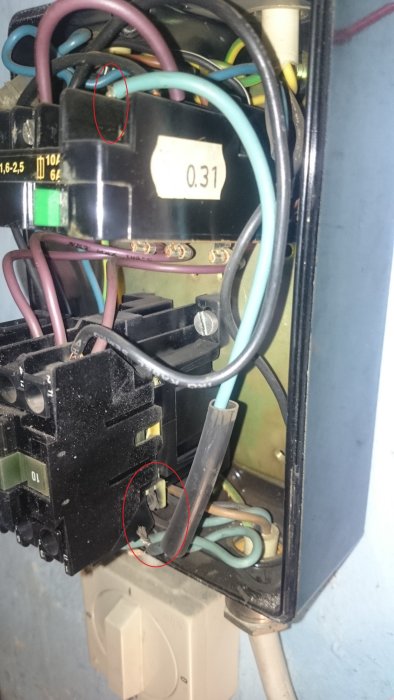 Öppet elektriskt motorskydd där en blå kabel är lös och markerad, nära svarta inkopplade kablar och potentiella brännskador.