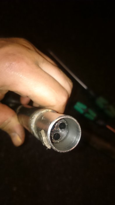 Hand håller pumpkontakt som inte går hela vägen på slangen mot mörk bakgrund.