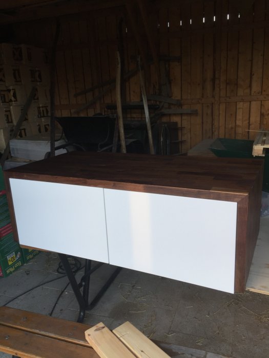 Hemsnickrad TV-möbel med mörkt trä och vita luckor står i en verkstad.