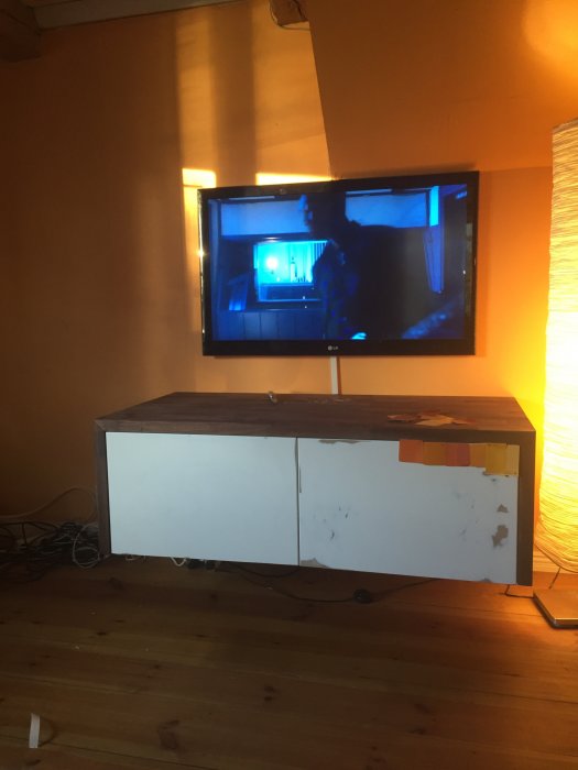 En hembyggd TV-möbel med vita luckor och trätopp, omgiven av färgprover på en vägg.