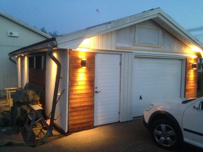 Garage exteriör på kvällen med nyinstallerade vägglampor som lyser upp fasaden.
