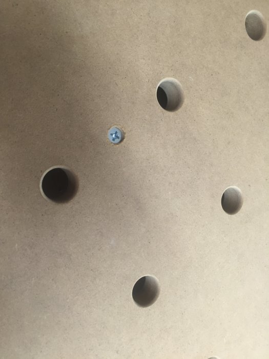 Närbild på en träskiva med borrade hål och en försänkt maskinskruv som fäster en fyrkantsprofil.