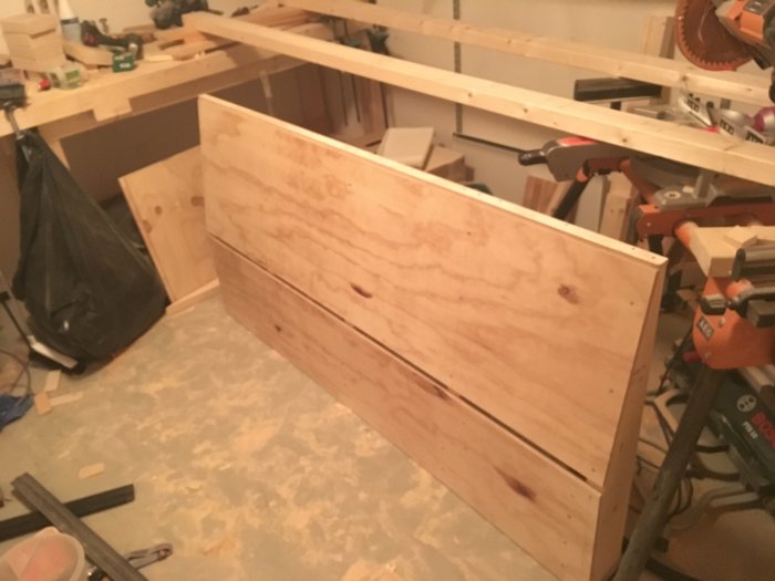 En plywoodgavel i ett verkstadsrum under tillverkning, med verktyg och byggmaterial i bakgrunden.