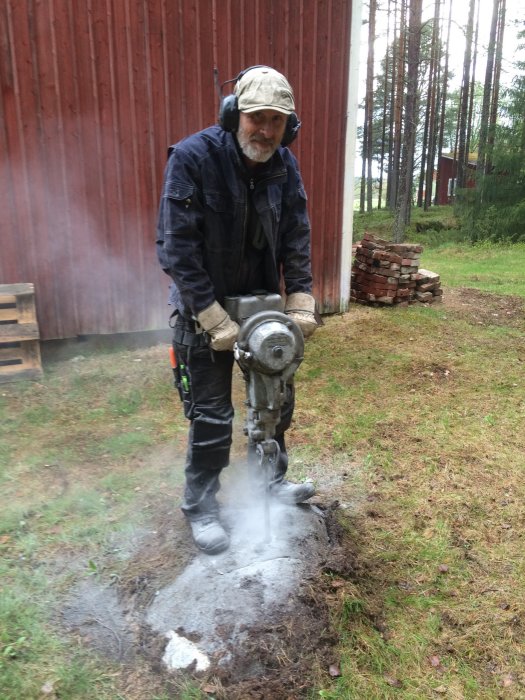 Person använder en äldre Cobra bergborr för att spränga sten nära en lada.