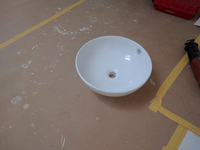 Ett oanvänt vitt tvättställ med 4.5 cm avloppshål på ett stökigt golv, till salu i Lund.