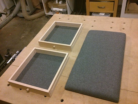 Två träramar bredvid en gråklädd sittdyna på en arbetsbänk.