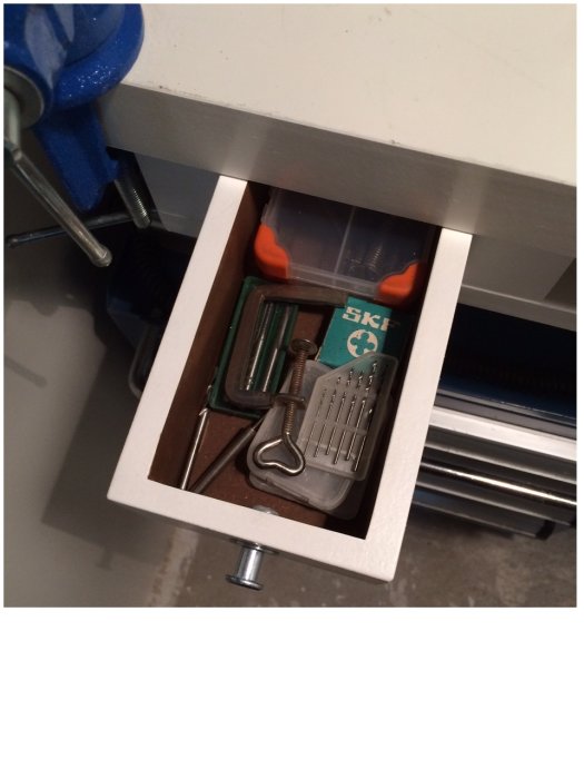 Öppen liten låda i arbetsbänk med verktyg såsom skruvmejsel och nycklar, i en finmekarhörna.
