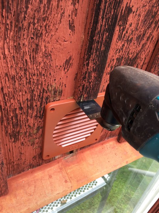 En borr förstärker ett snett hål i en röd vägg för att montera ett ventiltionsgaller.