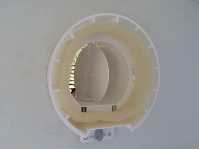 Ett snett borrat hål i en vägg med en installerad väggventil och gul isolering synlig runt kanterna.