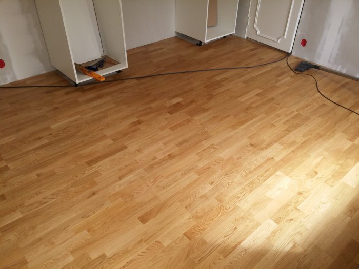Nyinstallerat parkettgolv med varierande marginaler runtom, utsågning nära elementet syns.