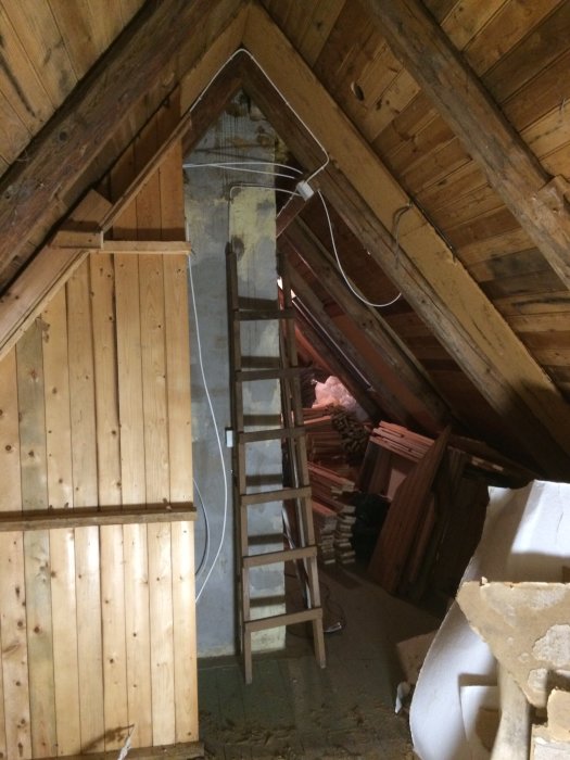 Attic under renovation with exposed wooden beams, a wooden ladder, and piles of removed wall materials.