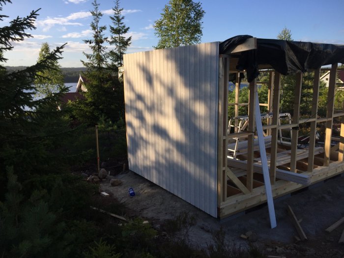 Hörn av en pågående byggnation med nyinstallerade falsade spårpaneler i solnedgång, med skog och en sjö i bakgrunden.